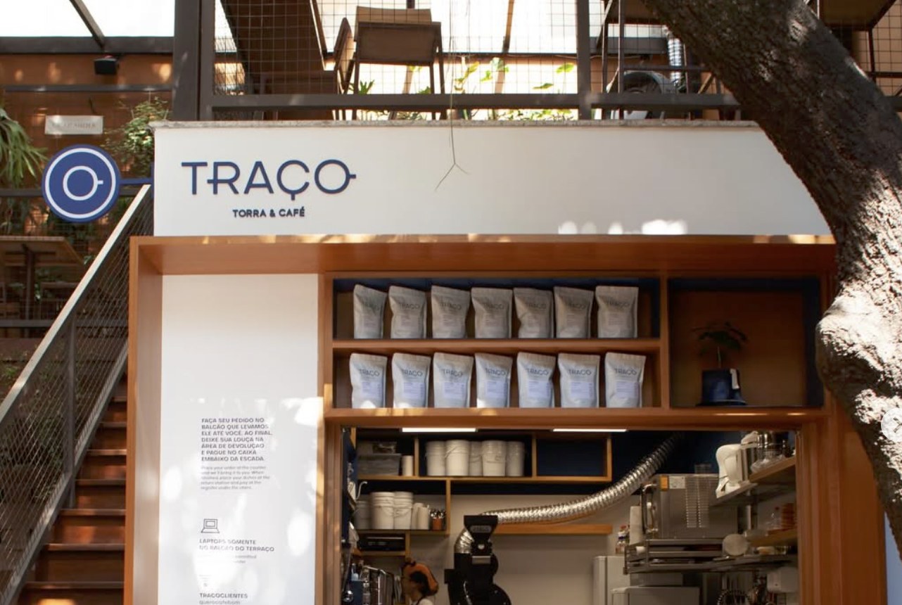 The kiosk counter and retail shelving at Traço Torra & Café, set beneath a tree